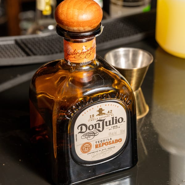 A bottle of Don Julio Reposado Tequila with a wooden cork, next to a cocktail glass.