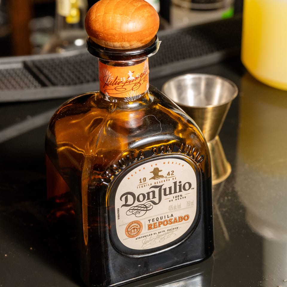 A bottle of Don Julio Reposado Tequila with a wooden cork, next to a cocktail glass.