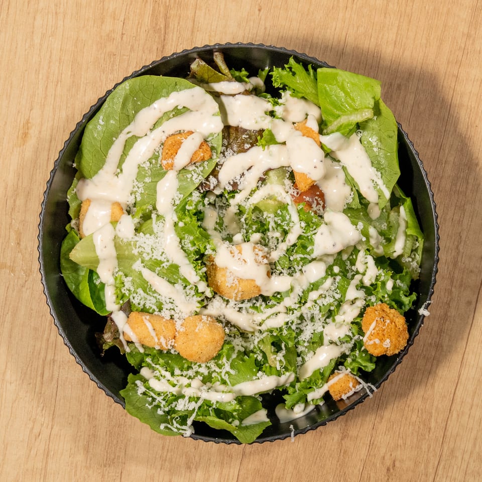 Overhead view of a Caesar salad with lettuce, croutons, parmesan cheese, and dressing in a black bowl.