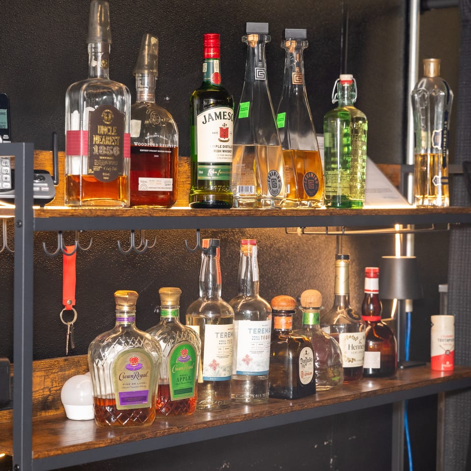 Two shelves display various liquor bottles, including whiskey, tequila, and other spirits, in a dimly lit bar area.