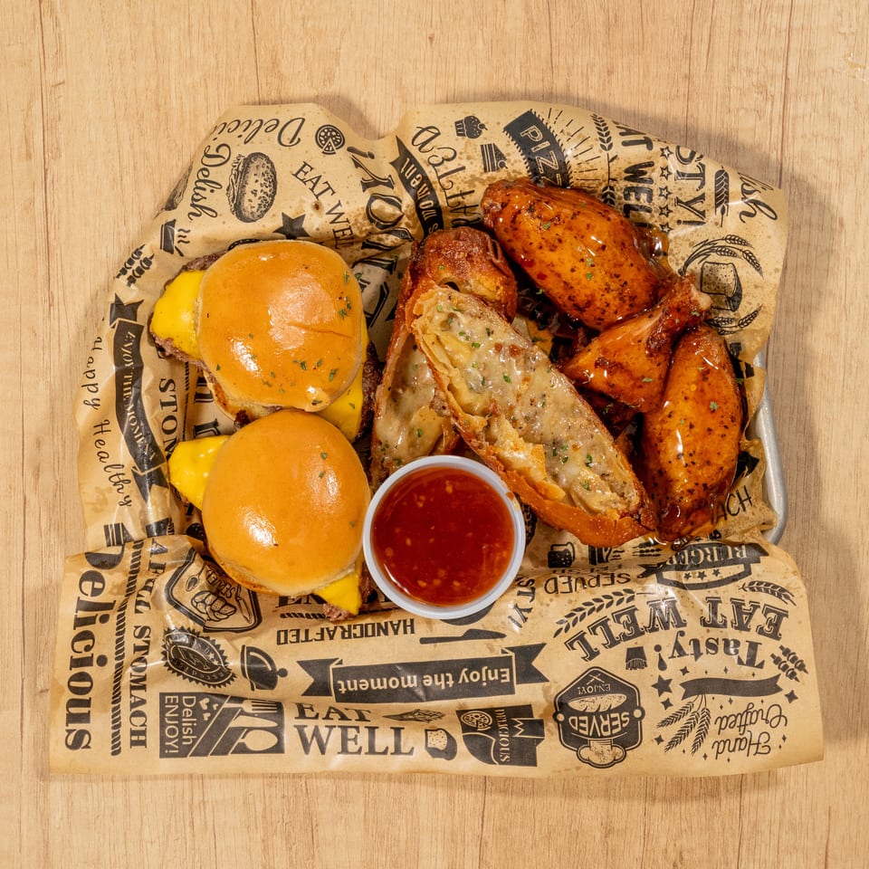 Two cheeseburger sliders, crispy chicken wings, and cheesy egg rolls with dipping sauce on a tray.