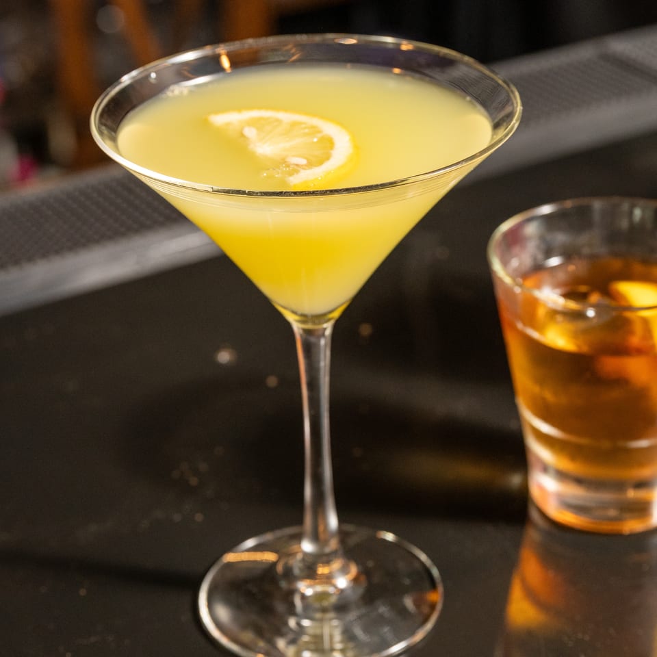A lemon drop martini and an Old Fashioned cocktail on a dark bar counter.