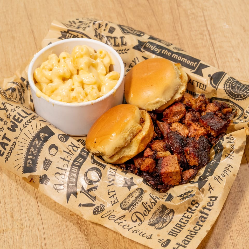 BBQ brisket burnt ends, two slider buns, and a side of mac and cheese on branded paper.